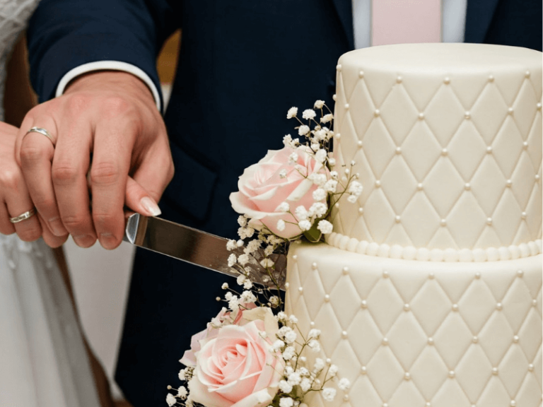 Un gateau mariage sophistiqué à étages, sublimé par un glaçage lisse et des décorations florales pastel, présenté sur une table rustique dans une ambiance romantique. Idéal pour illustrer une recette de gâteau de mariage fait maison, alliant raffinement et simplicité.
